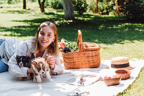 happy blonde girl sitting on blanket in garden and having picnic with puppies at sunny day
