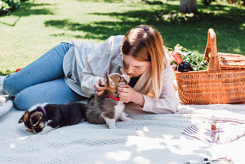 blonde girl sitting on blanket in garden and playing with puppies at sunny day