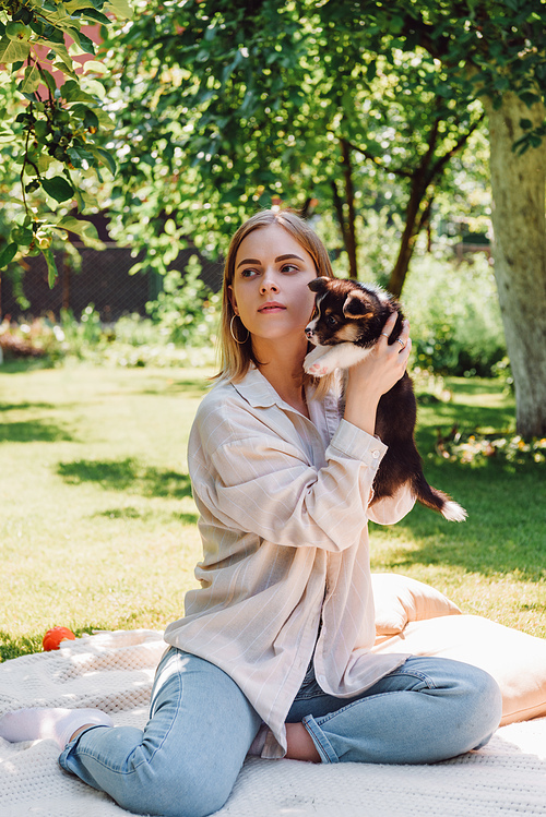 blonde girl with closed eyes holding cute puppy in green garden and looking away