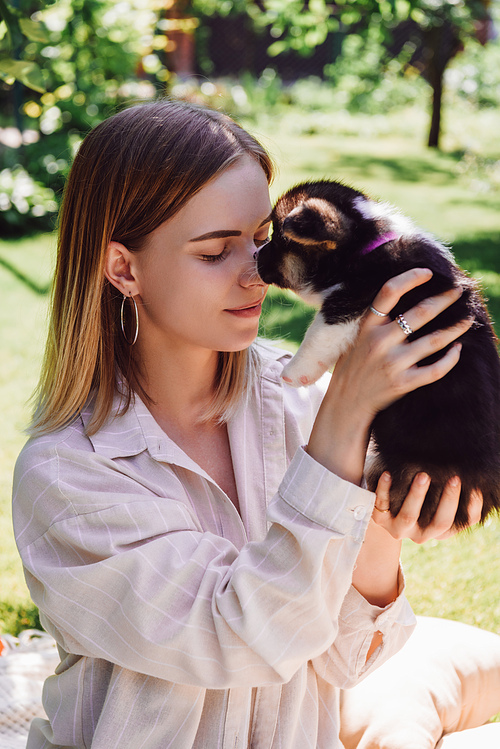 smiling blonde girl with closed eyes holding cute puppy in green garden