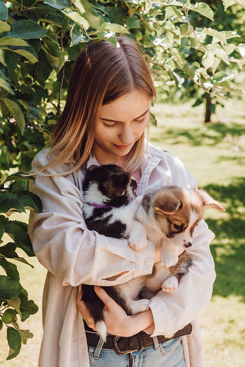 blonde girl holding cute puppies in garden near green tree