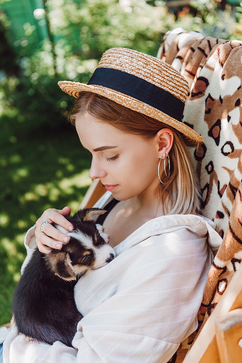 blonde girl in straw hat holding puppy while sitting in deck chair in garden