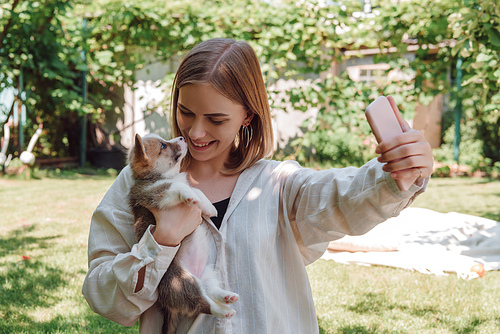 blonde girl in green garden taking selfie with adorable puppy