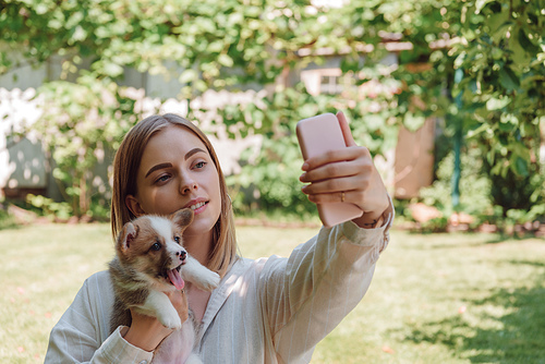 blonde girl in green garden taking selfie with cute puppy