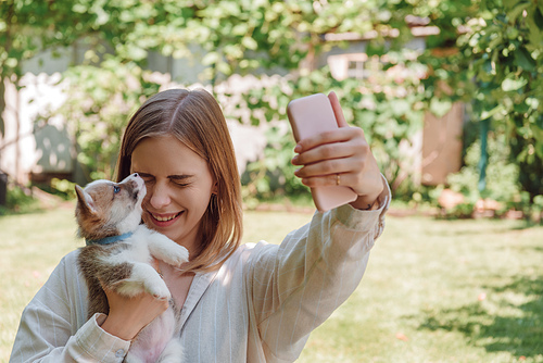 blonde girl in green garden taking selfie with closed eyes and adorable puppy