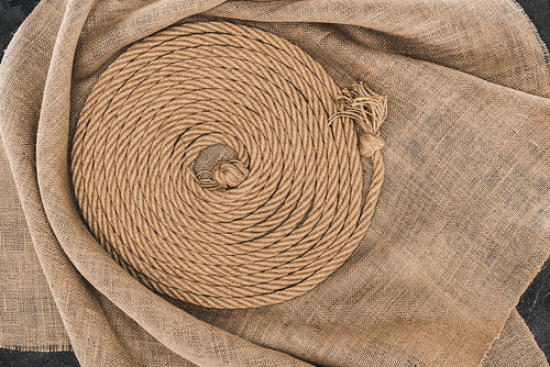 top view of brown nautical rope arranged in circle on sackcloth on dark concrete surface