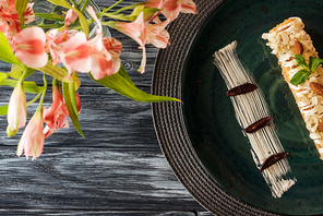 top view of delicious dessert with almonds on plate and flowers on wooden table