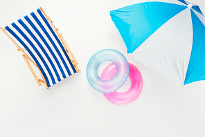 top view of beach umbrella| striped beach chair and inflatable rings isolated on white