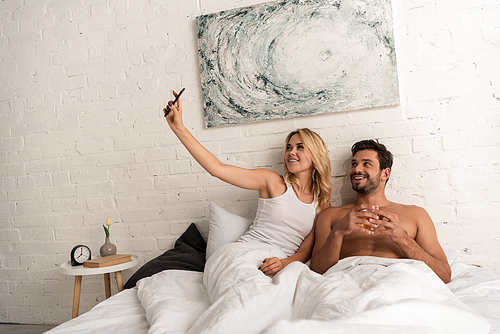 beautiful smiling couple taking selfie on smartphone in bed in the morning
