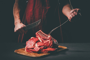 butcher with fork and knife cutting raw meat on wooden cutting board