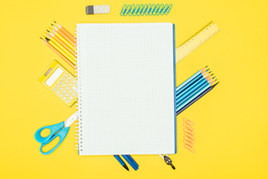Top view of composition of colorful school supplies with blank notebook isolated on yellow background