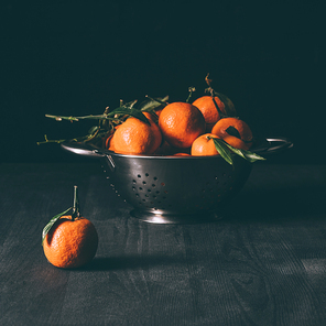 close up view of pile of mandarins with leaves in strainer on dark wooden tabletop