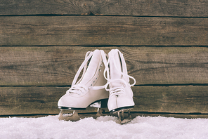 pair of white skates on snow near wooden wall