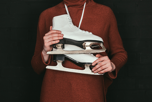 cropped image of woman in brown sweater holding skates isolated on black