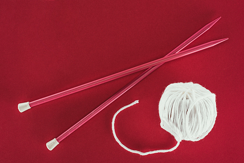 top view of white wool ball and knitting needles| isolated on red