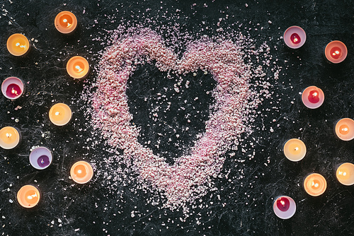 top view of heart shaped pink 씨솔트 and candles on black marble surface| aroma therapy concept