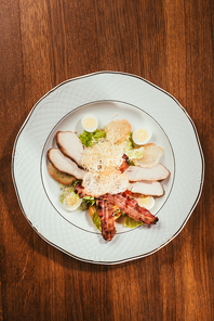 view of ham slices with fried meat and some boiled eggs on plate over wooden surface