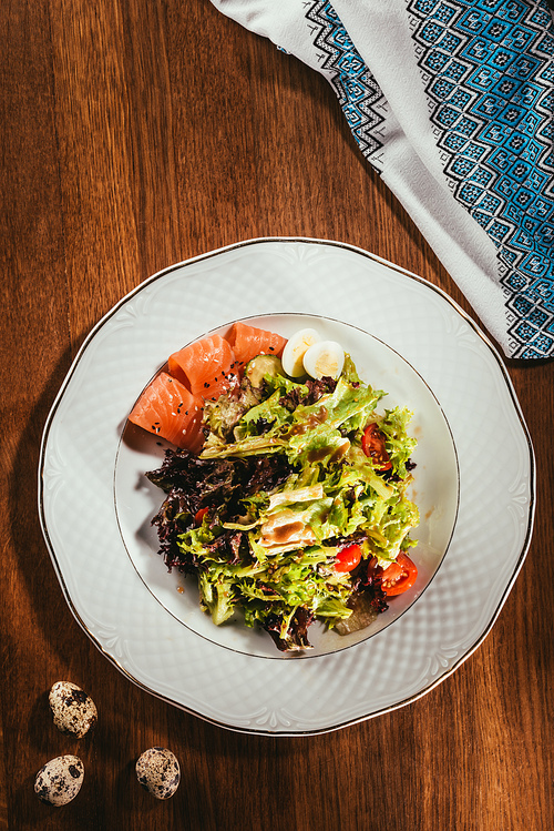 Top view of fresh salad with vegetables| eggs and salmon served on white plate with napkin on wooden table