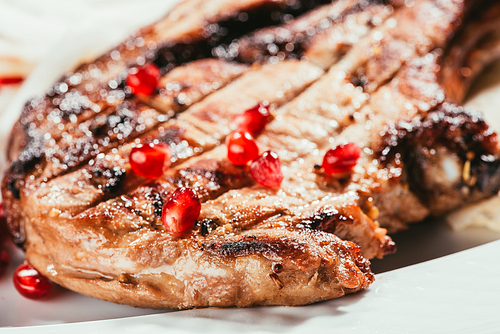 Close-up view of grilled meat with pomegranate seeds on white plate