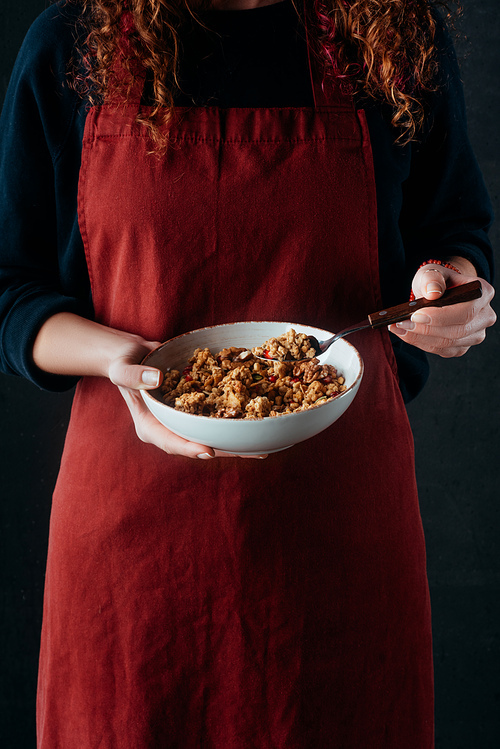 cropped image of female cook holding bowl with granola and spoon