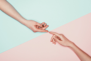 cropped shot of women touching fingers on halved pink and turquoise surface