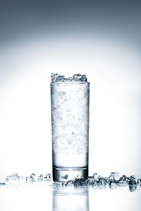 glass of cold water with crushed ice on reflective surface on white