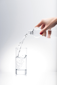 cropped shot of woman pouring water into glass from plastic bottle