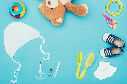 top view of teddy bear and baby clothes with equipment isolated on blue