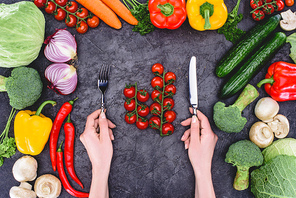 cropped shot of person holding fork and knife above healthy fresh vegetables on black