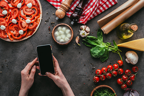 cropped shot of woman using smartphone while preparing pizza on concrete table