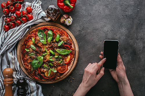 cropped shot of woman using smartphone on concrete table with pizza