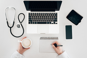 partial view of doctor at workplace with laptop| stethoscope and cup of coffee