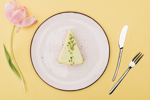 top view of piece of cake on plate| tulip flower and cutlery isolated on yellow