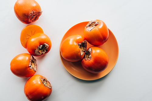 top view of persimmons on orange plate and on white tabletop