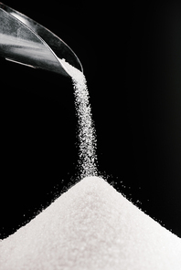 white sugar falling from metal scoop on pile isolated on black