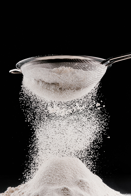 white flour falling from sieve on pile isolated on black