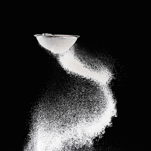 sieve with falling flour isolated on black