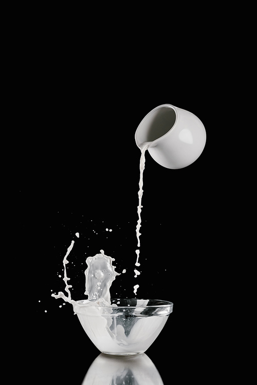 milk pouring from milk jar into bowl on black