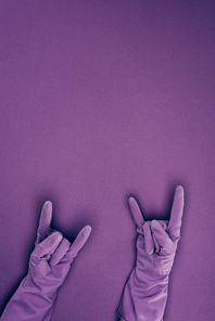 cropped image of woman showing rock signs in rubber protective gloves isolated on violet
