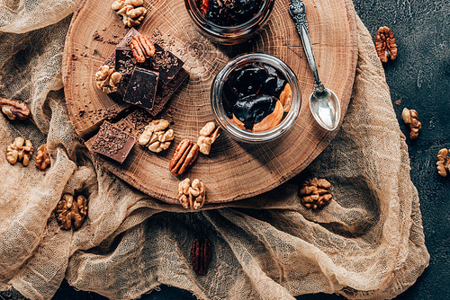 top view of delicious dessert in glass jars and chocolate pieces with nuts on wooden board