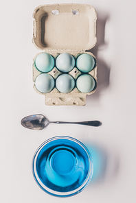 top view of glass with blue paint| spoon and chicken eggs in tray| easter concept