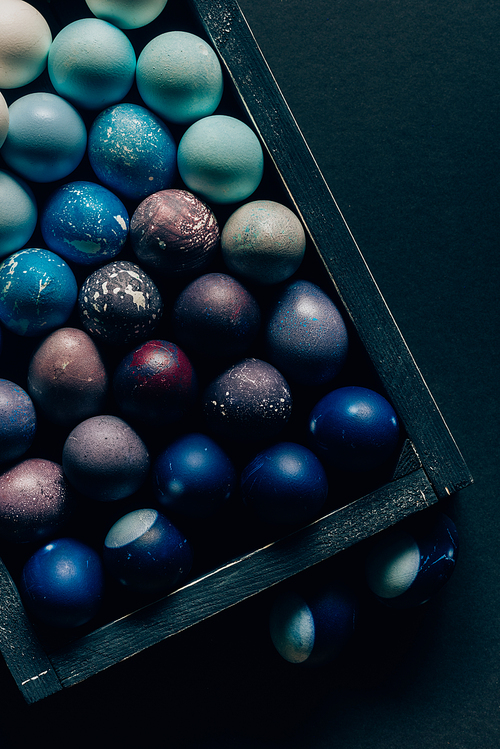 top view of colored painted easter eggs in wooden box on dark table