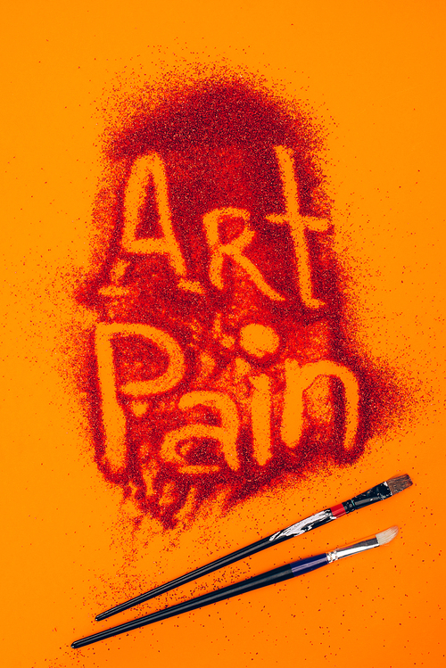 top view of art pain sign made of red sand and brushes isolated on orange