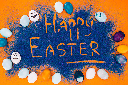 top view of happy easter sign made of blue sand with painted eggs on orange