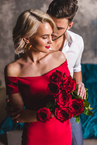 handsome man hugging smiling sensual woman in red dress holding beautiful roses