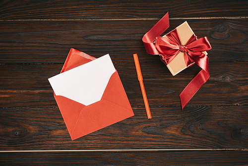 top view of red envelope with blank paper and gift box on wooden table