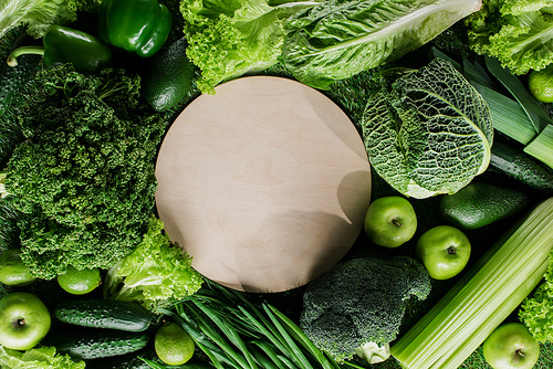 top view of round wooden board between green vegetables| healthy eating concept