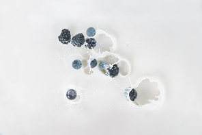 Drops of milk with raw berries on white background