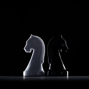 silhouettes of white and black chess knights isolated on black, business concept
