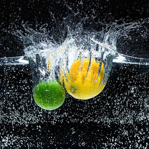 close up view of fresh lemons and limes in water isolated on black